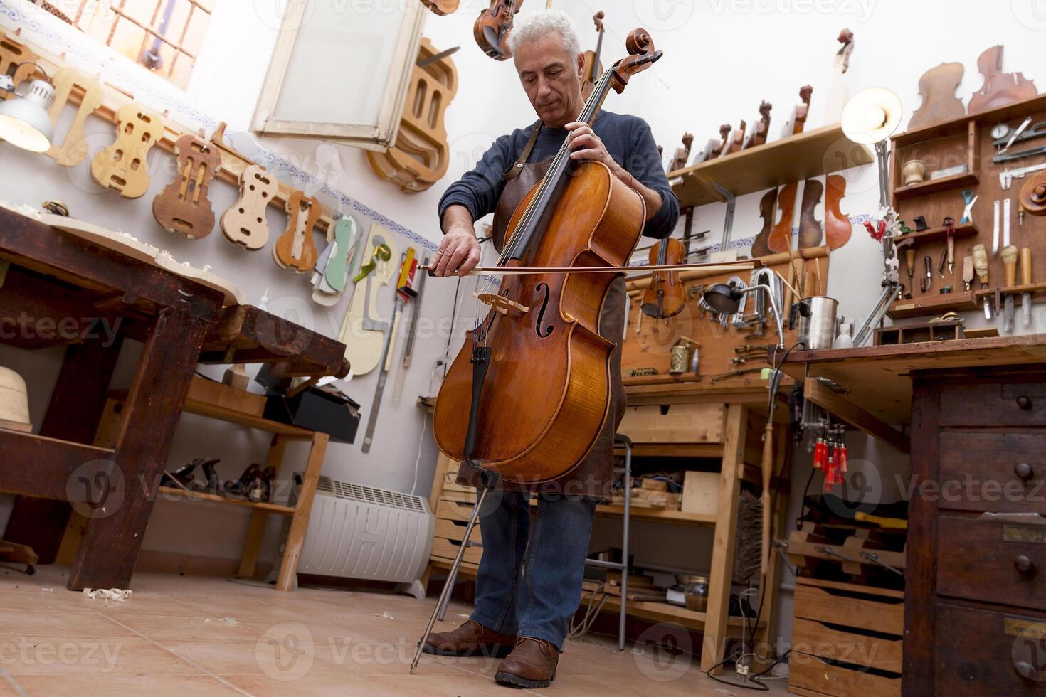 mature violin maker craftsman playing a newly made viola using the bow to hear the sound at the workplace photo