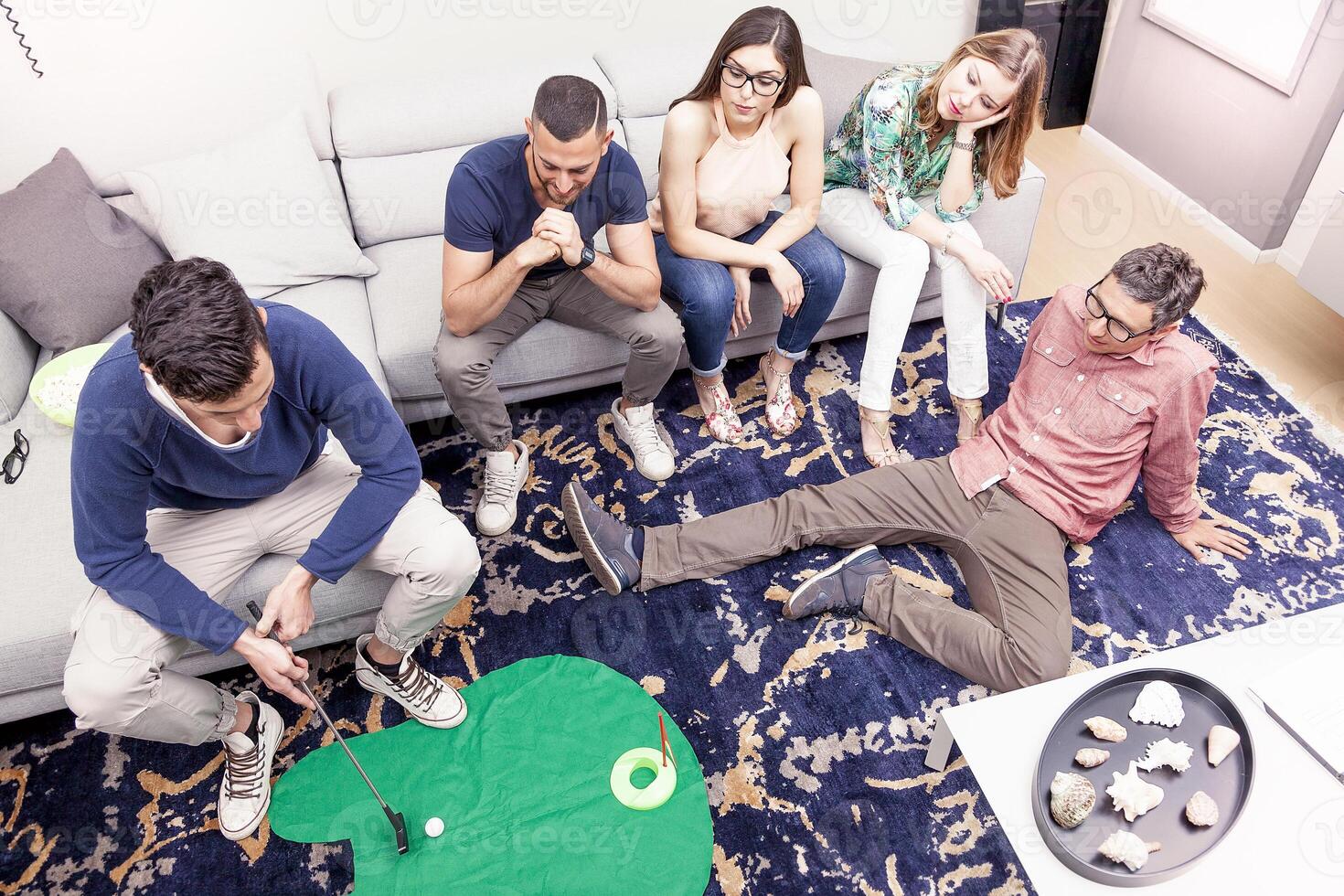 top view of group of young male and female friends playing golf on floor at home photo