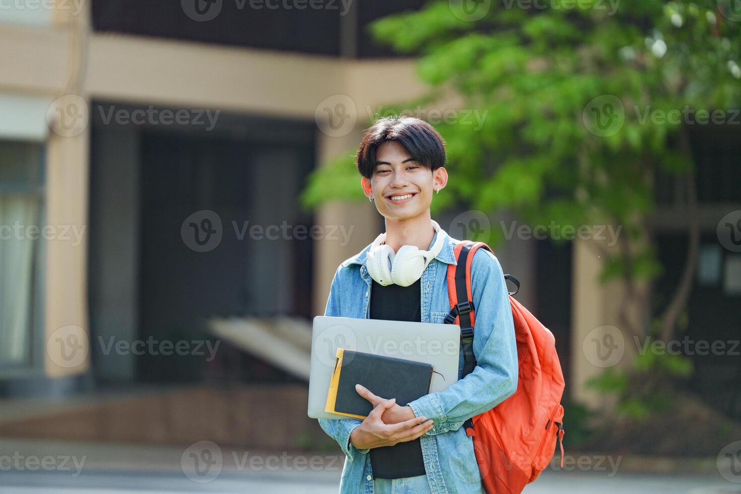 A cheerful Asian college student stands outside on campus with a backpack, smiling and looking at the camera. photo