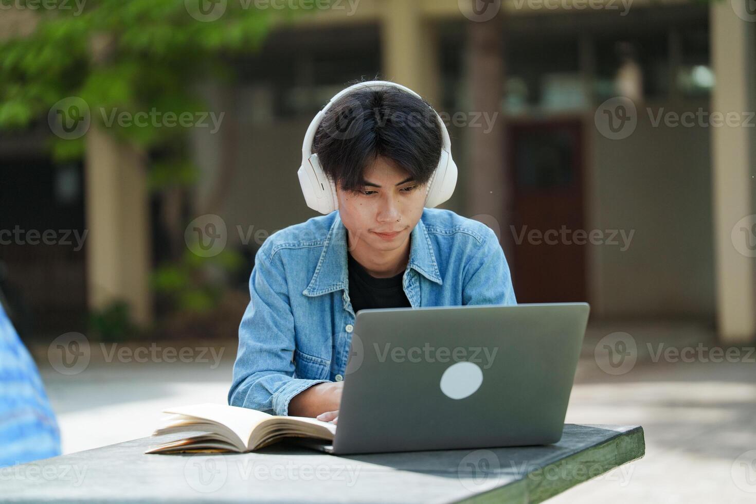 Portrait of a young college student sitting and using laptop on the bench on campus. photo