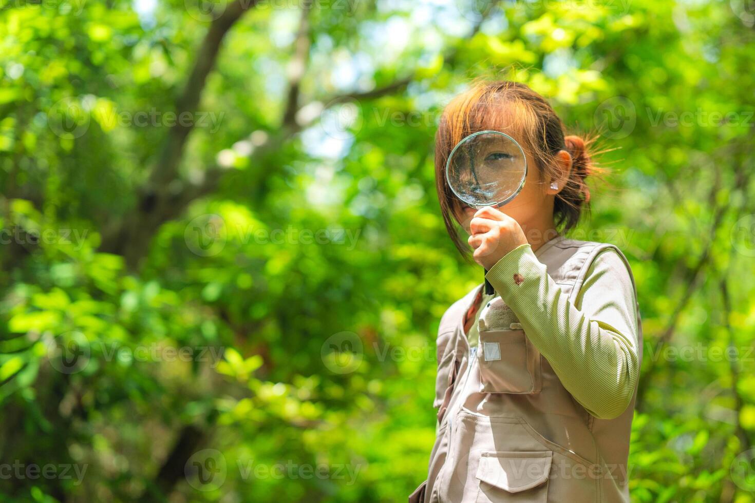 Happy little girl is exploring in the forest and looking for insects with a magnifying glass. Adventure tourism and learning concept. photo