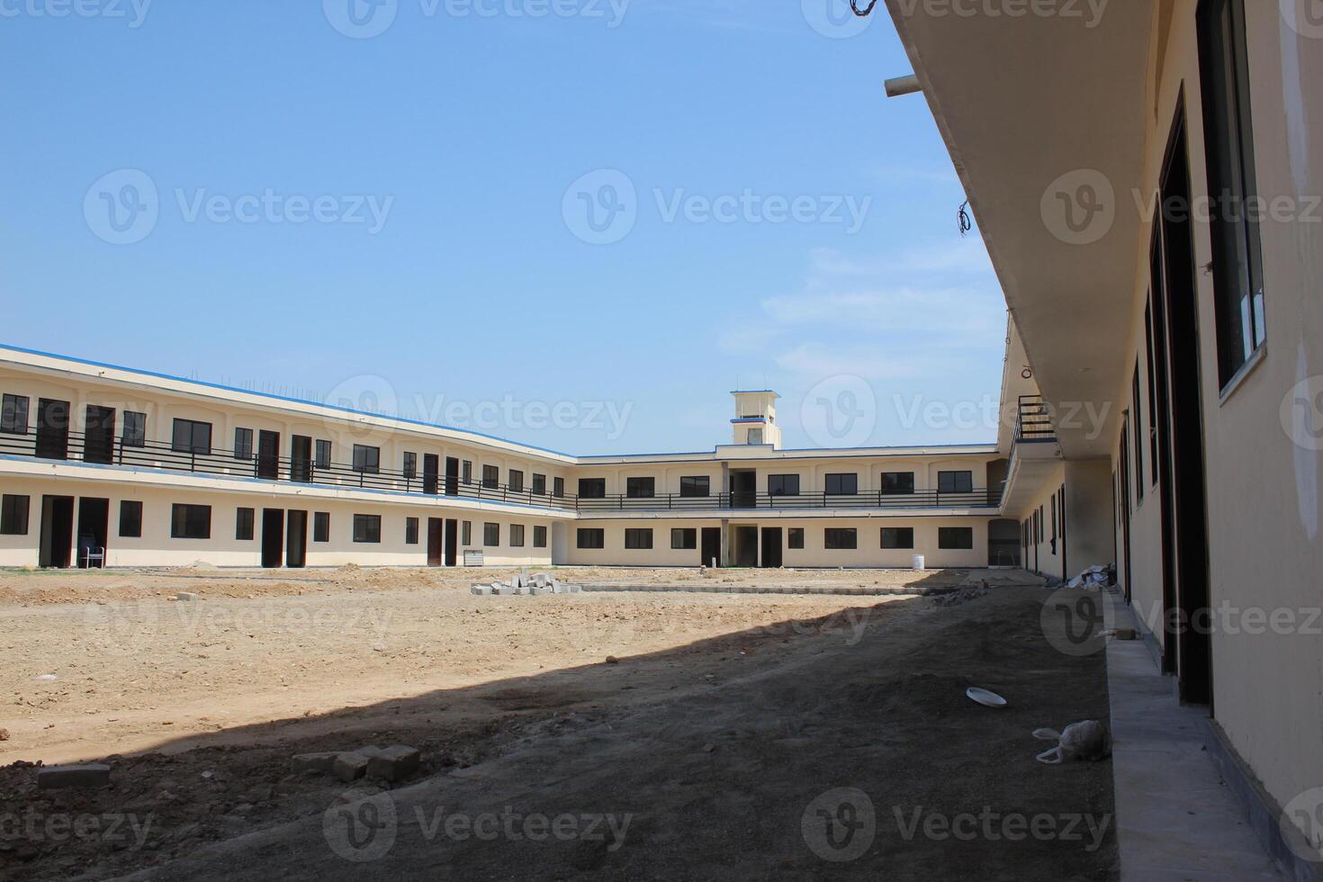 School building with two stories, having cream-colored walls and a flat roof, arranged in a U-shape with an open courtyard in the center. photo