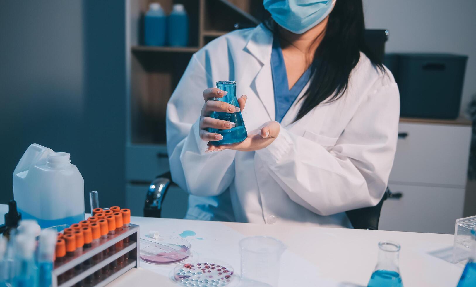 A woman in a lab coat holding a vial of liquid photo