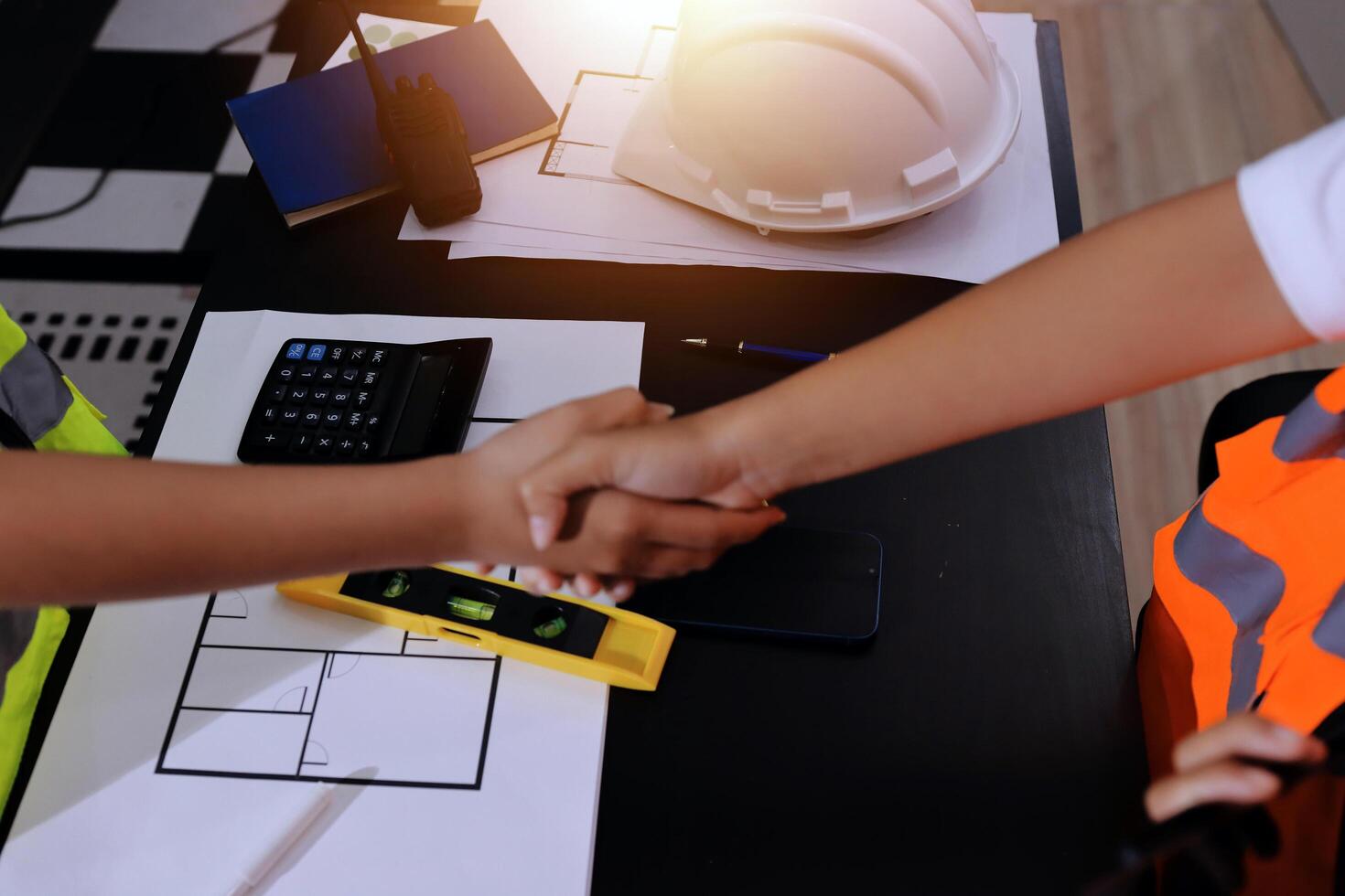 Two people shaking hands at a desk with construction tools photo