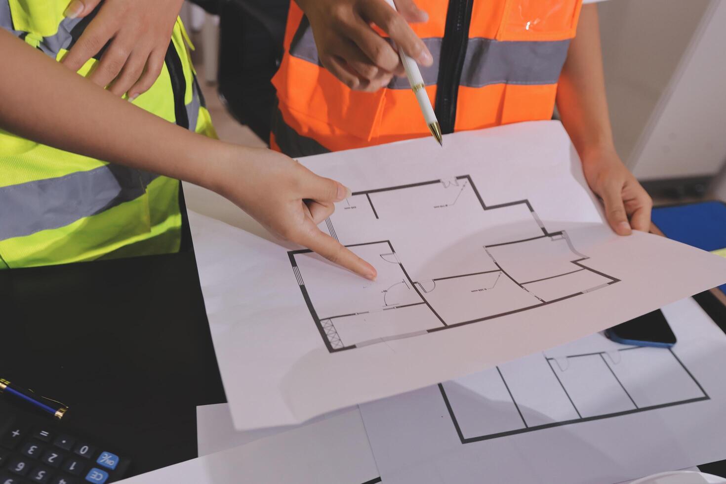 Two people in safety vests are looking at a blueprint photo