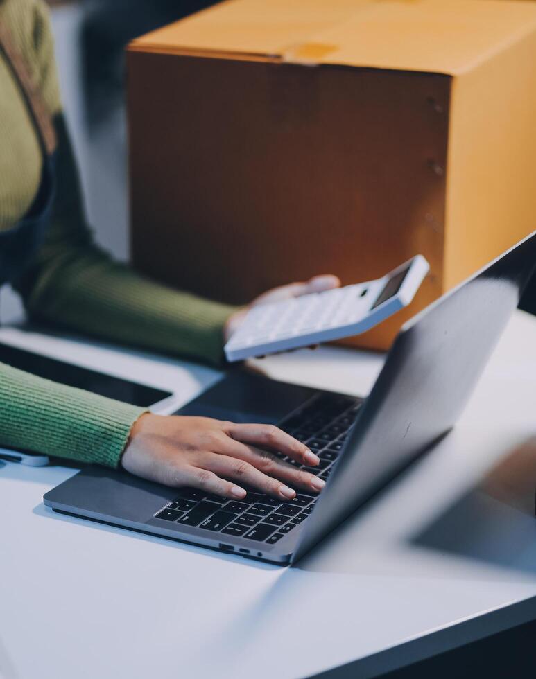 A woman is typing on her laptop while holding a box photo