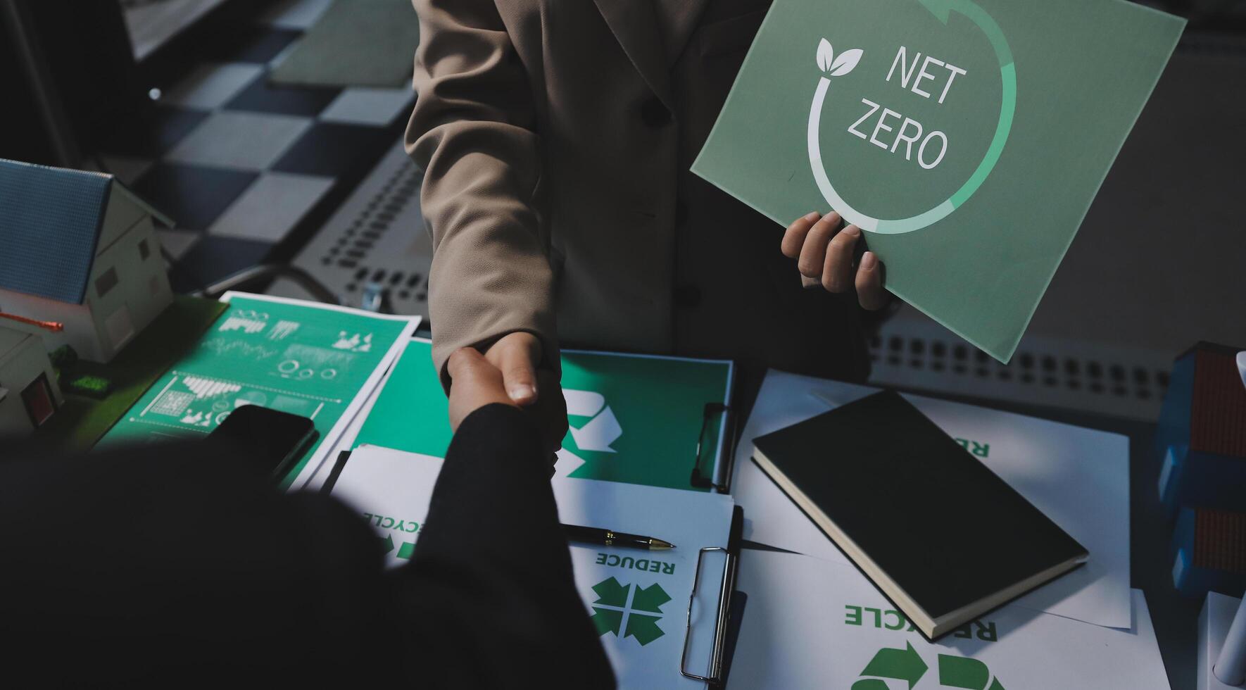 A man and woman shaking hands with a net zero sign photo