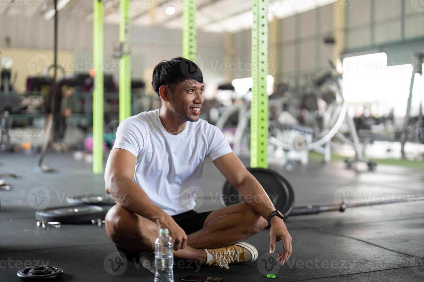 Fitness and Motivation. Young man smiling while resting in gym after workout. photo