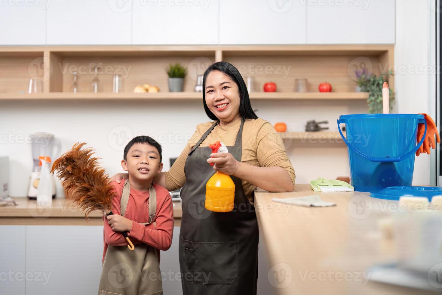 Family Cleaning Day. A mother and son posing with cleaning tools in a bright kitchen. photo