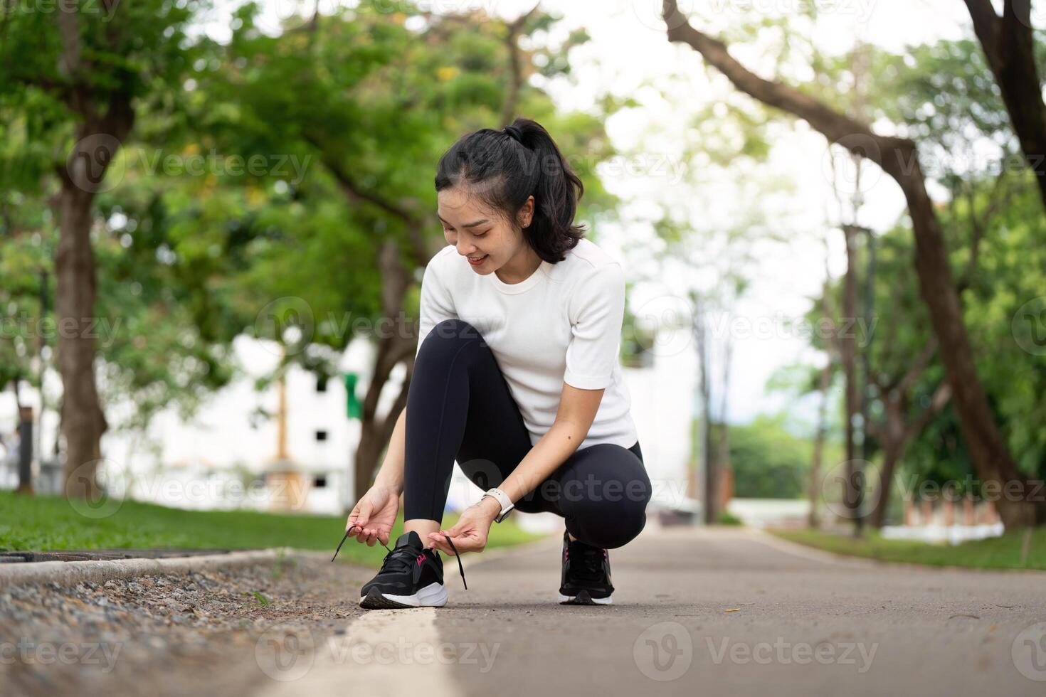 Active Lifestyle. Young woman tying shoelaces before running outdoors in a park. photo