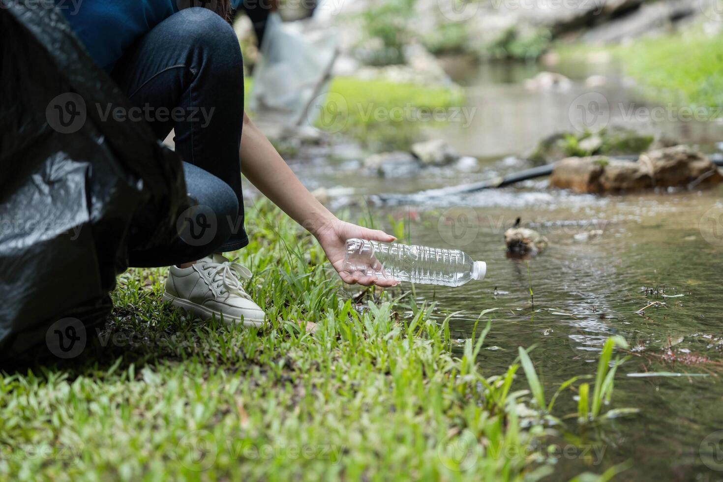 Plastic Waste Removal from Water. A volunteer carefully retrieves a plastic bottle from a stream during a cleanup effort. photo