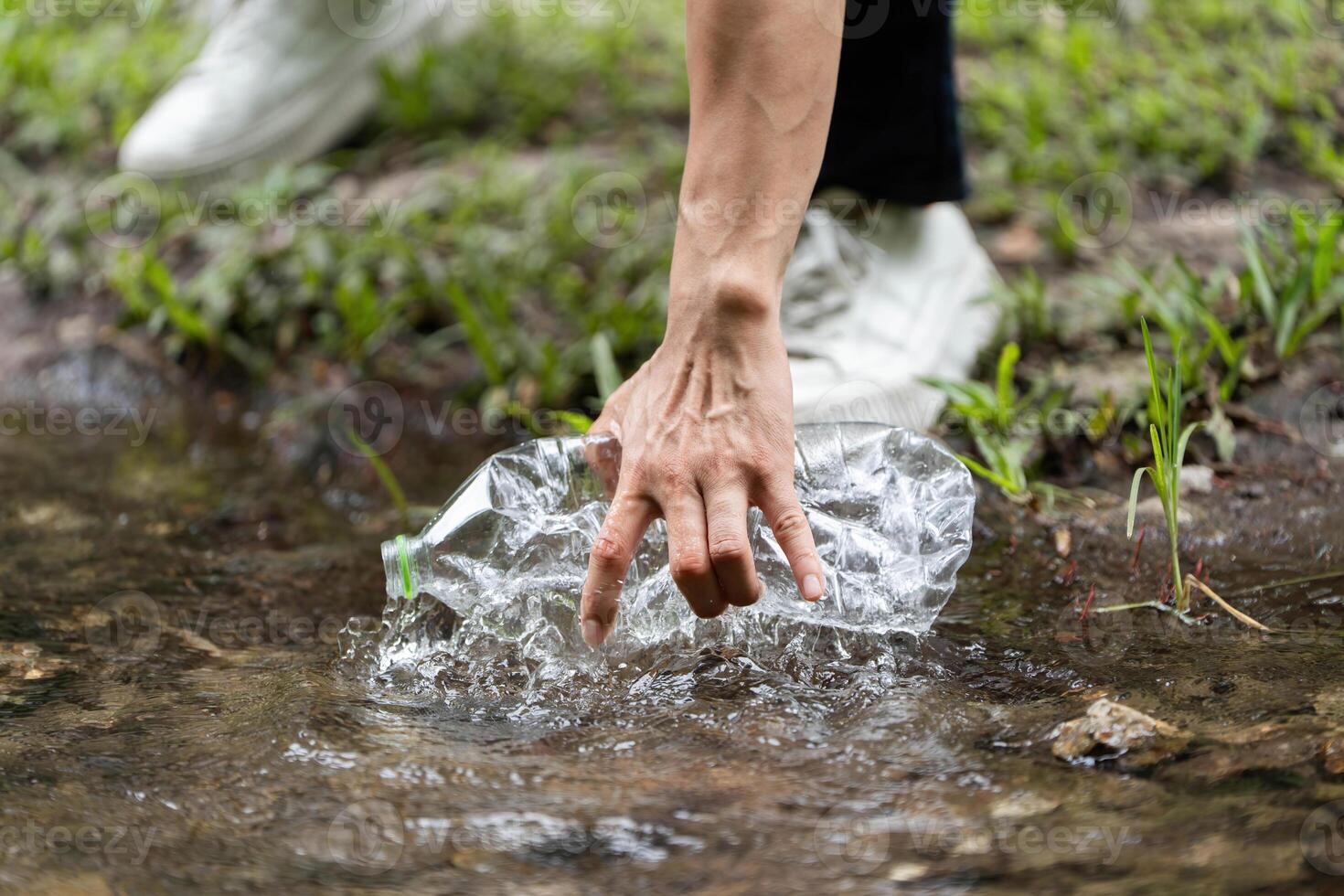 Volunteer action. Individual retrieving plastic bottle from river. photo