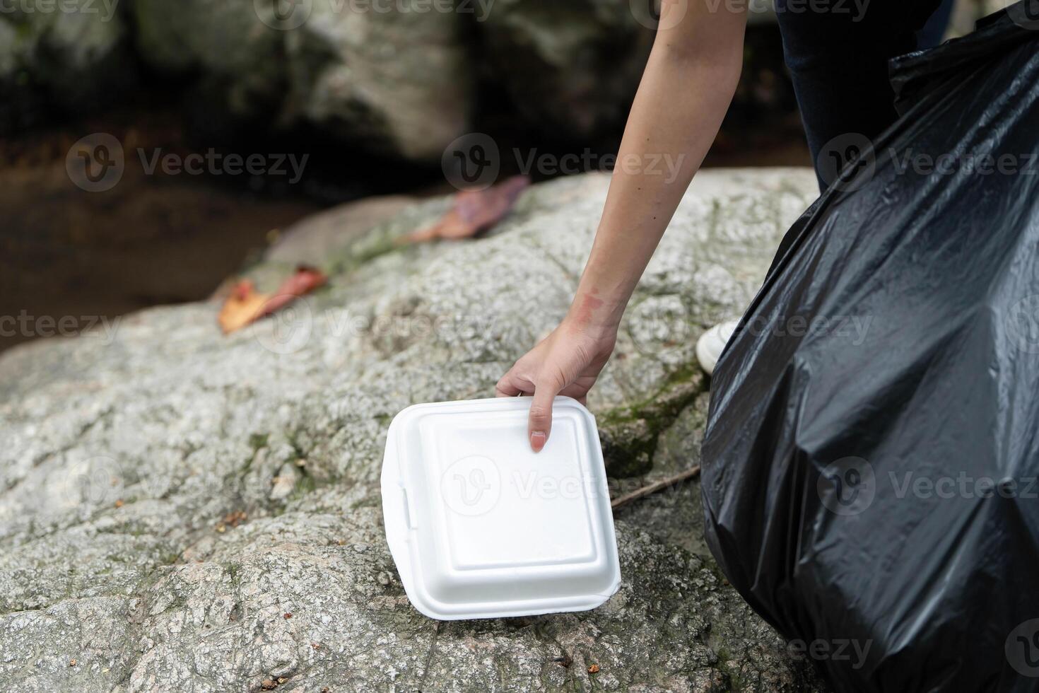 Individual Picking Up Food Container During Clean-Up. Volunteer collecting waste from rocky area. photo