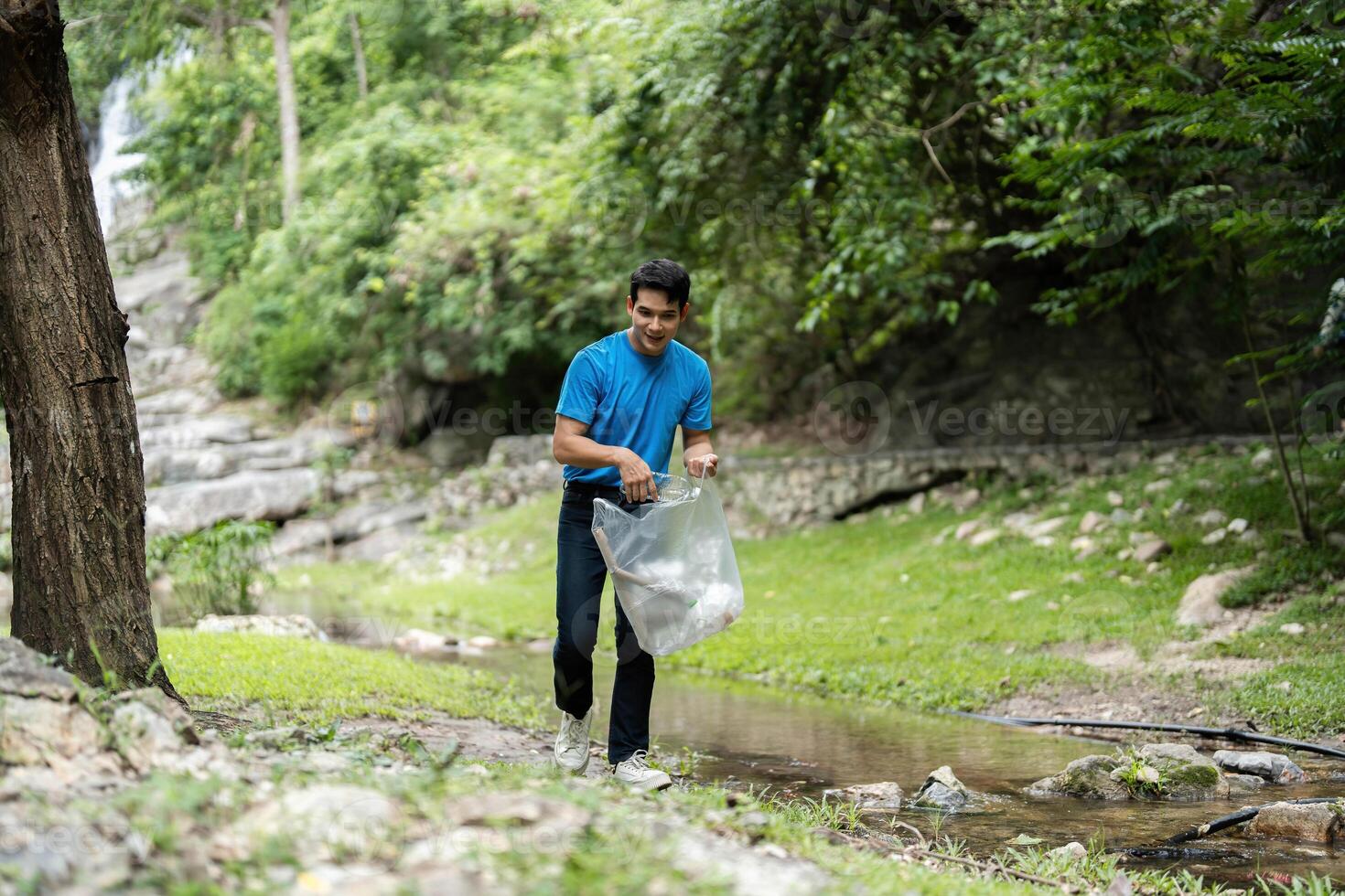 Volunteer in action. Young man collecting litter by the stream. photo