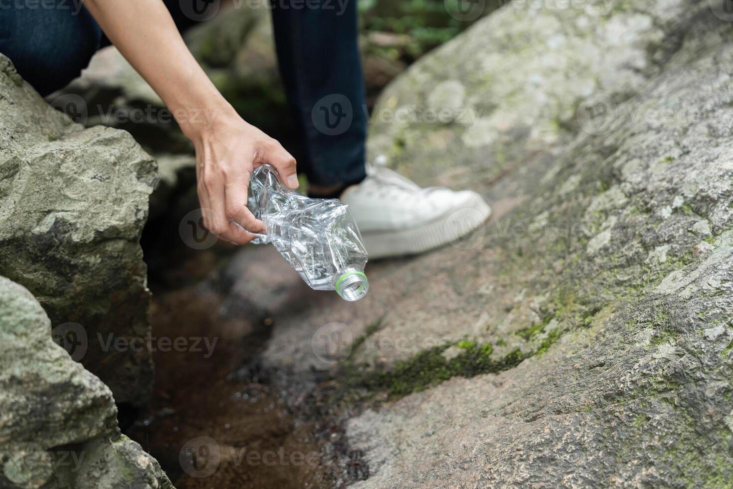 Individual Picking Up Plastic Bottle from Rocks. Volunteer actively engaging in environmental cleanup by removing litter. photo