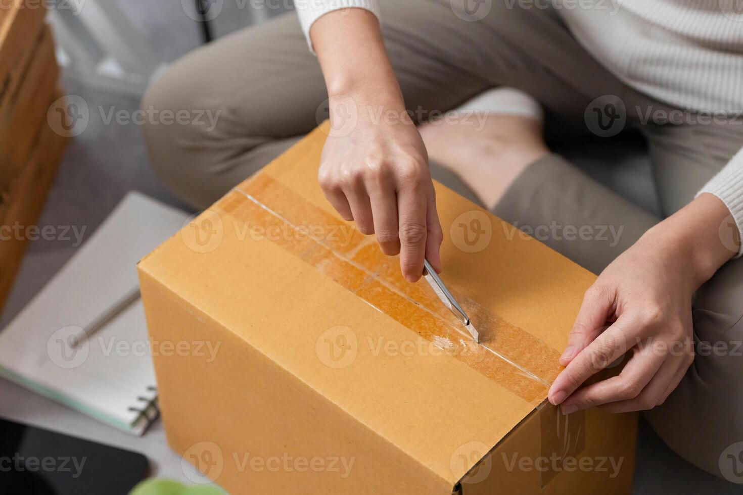 Moving tasks. Woman using a utility knife to open a delivery box. photo