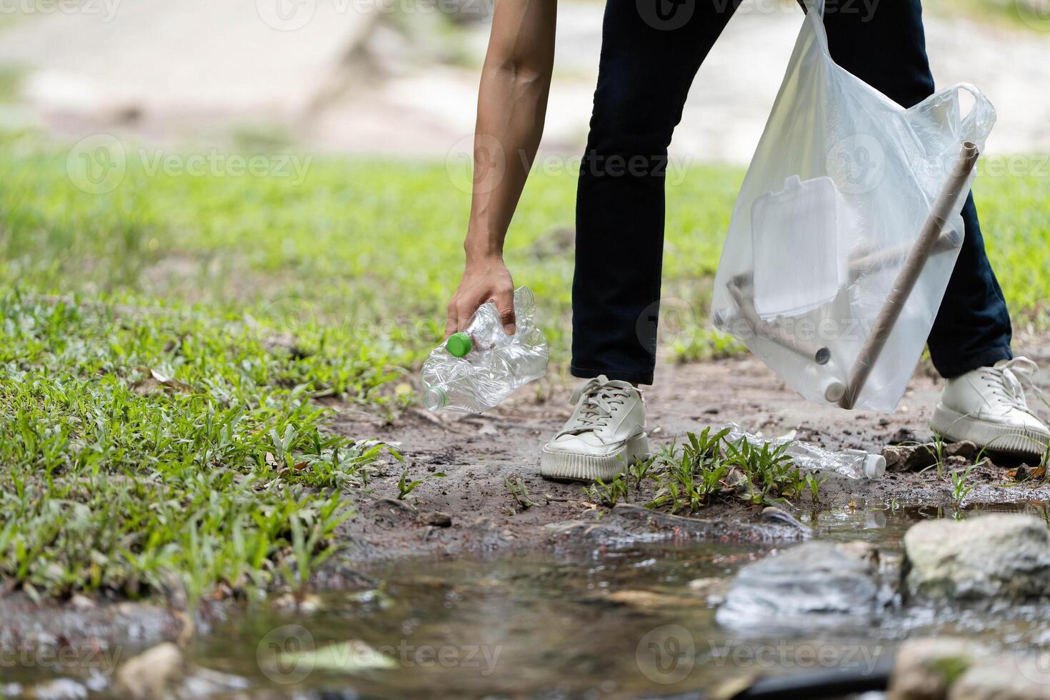 Nature Conservation Efforts. A volunteer picking up plastic bottles near a stream. photo