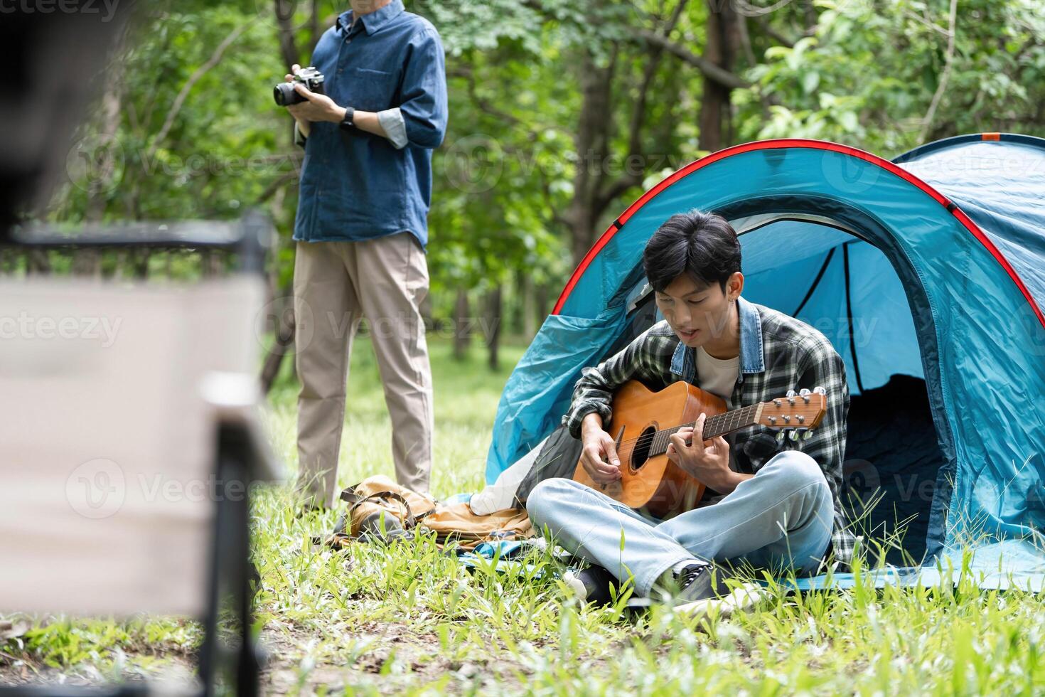 Family bonding outdoors. Young man playing guitar while father captures moments with camera. photo
