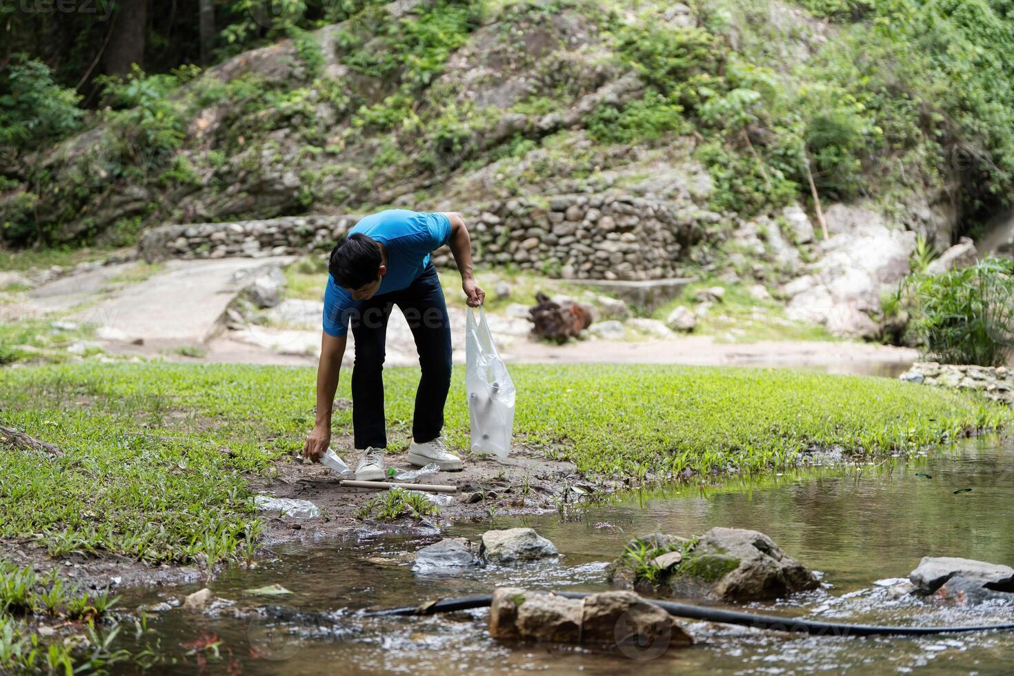 Volunteer Picking Up Waste. A young man collects plastic from a stream during a clean-up event. photo