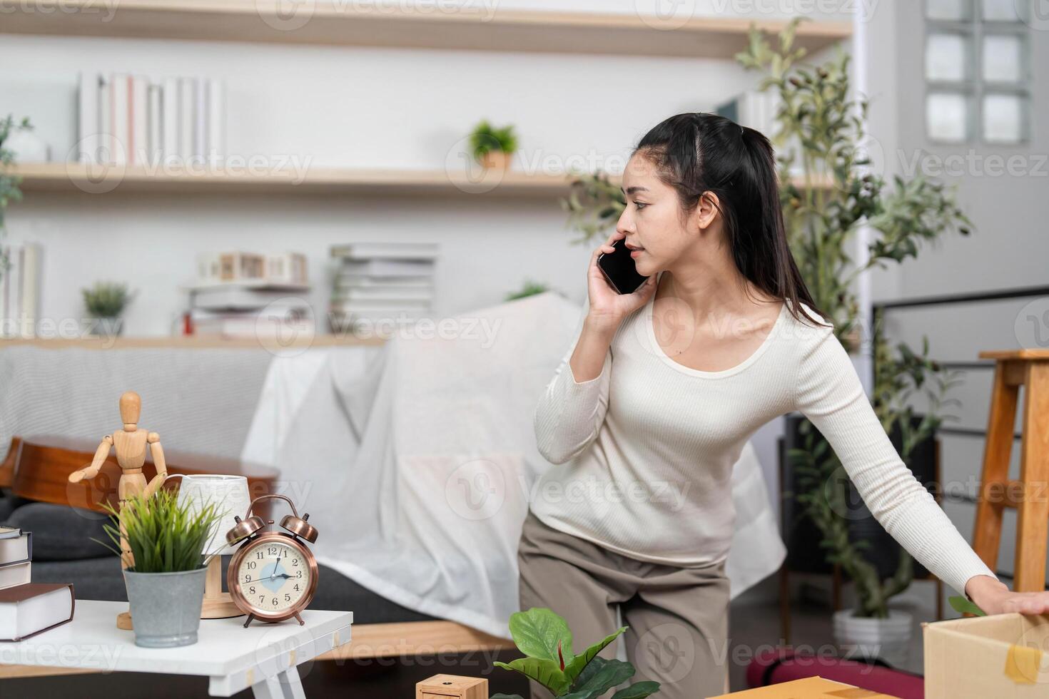 Moving and Multitasking. Young woman on phone while arranging boxes in her living space. photo