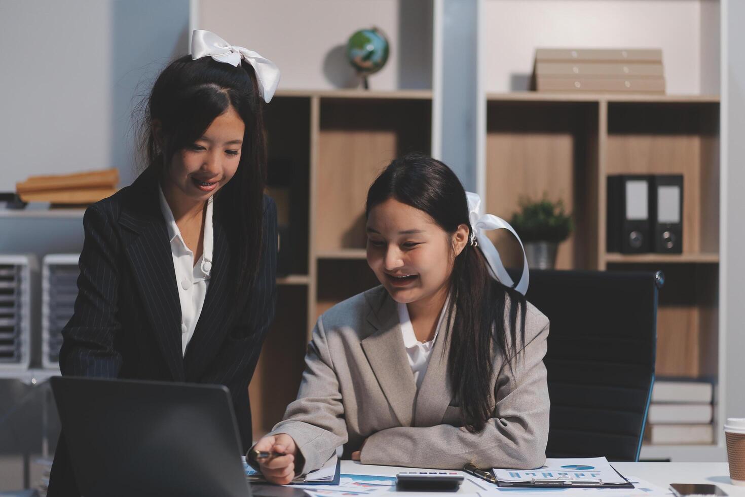 Two asian girls in business attire working on a laptop photo