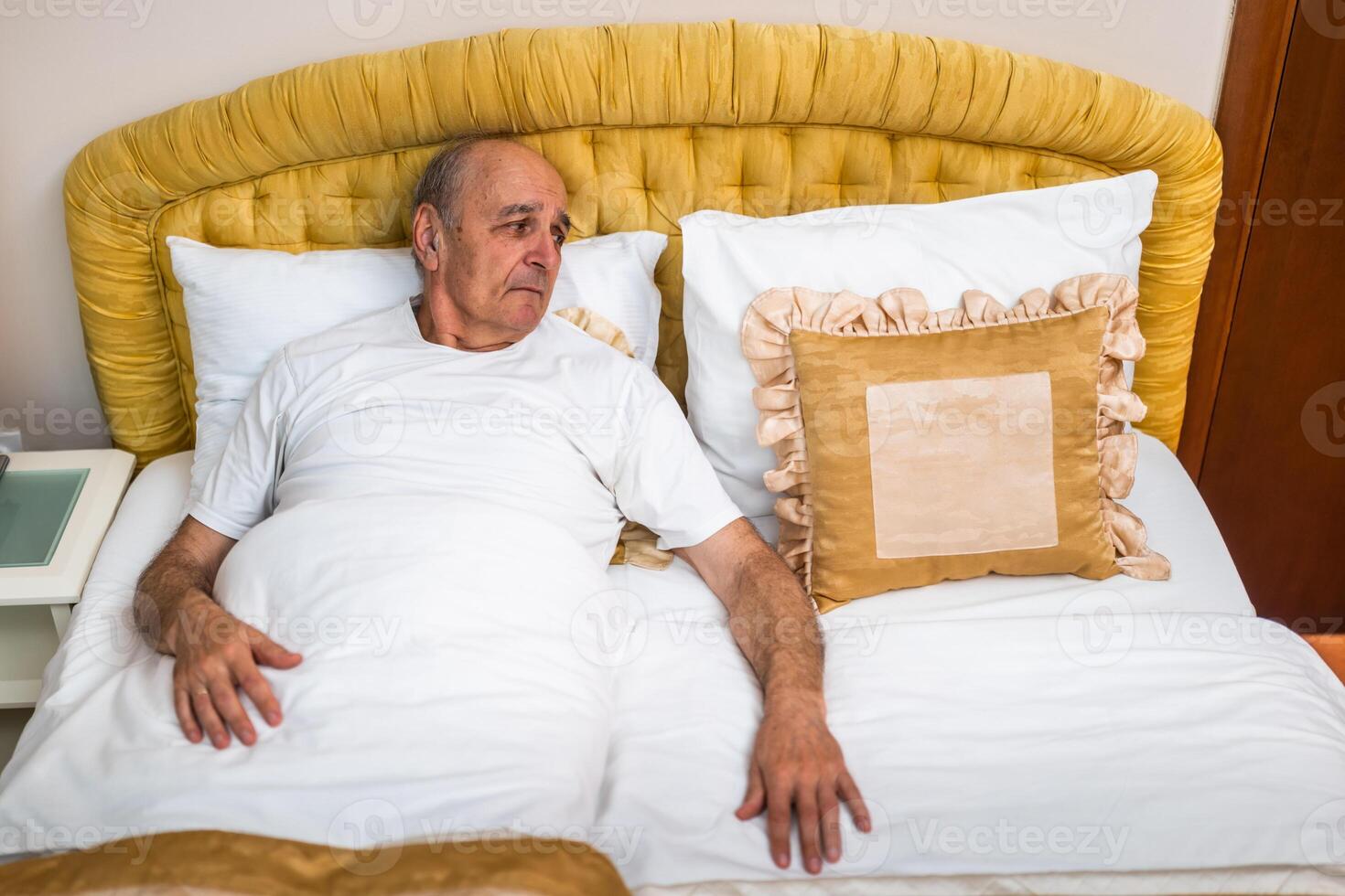 Lonely senior man waking up alone in bed, looking away in silence and expressing sadness. Deeply emotional portrayal of aging and grief. photo