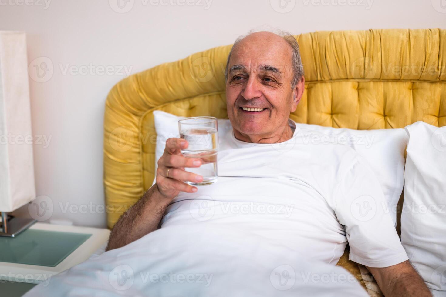 Comfortable senior in bed, wearing cozy sleepwear, sipping water as part of his daily morning health care routine. photo