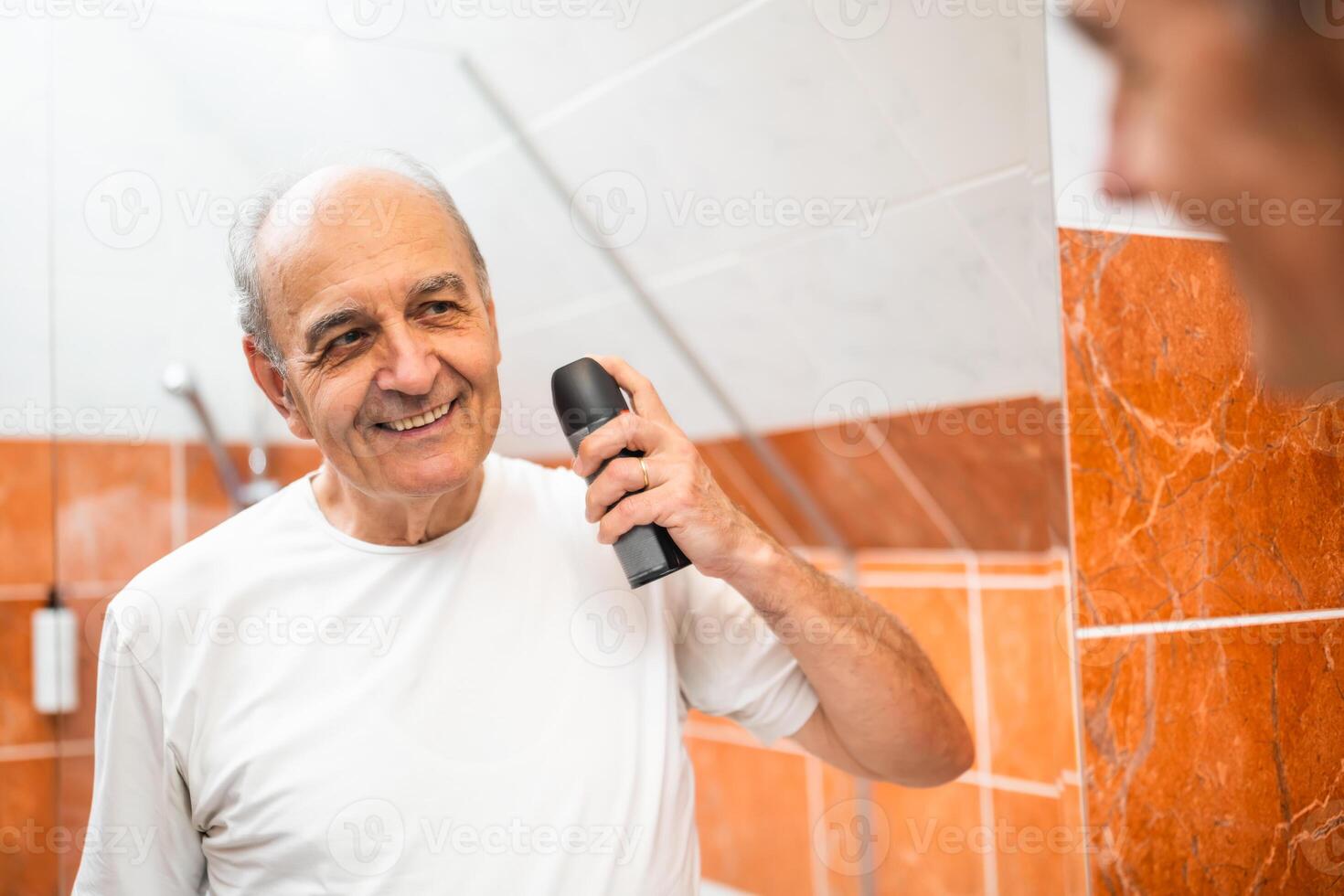 Relaxed elderly man taking time for personal grooming, applying a refreshing deodorant spray with joy. photo