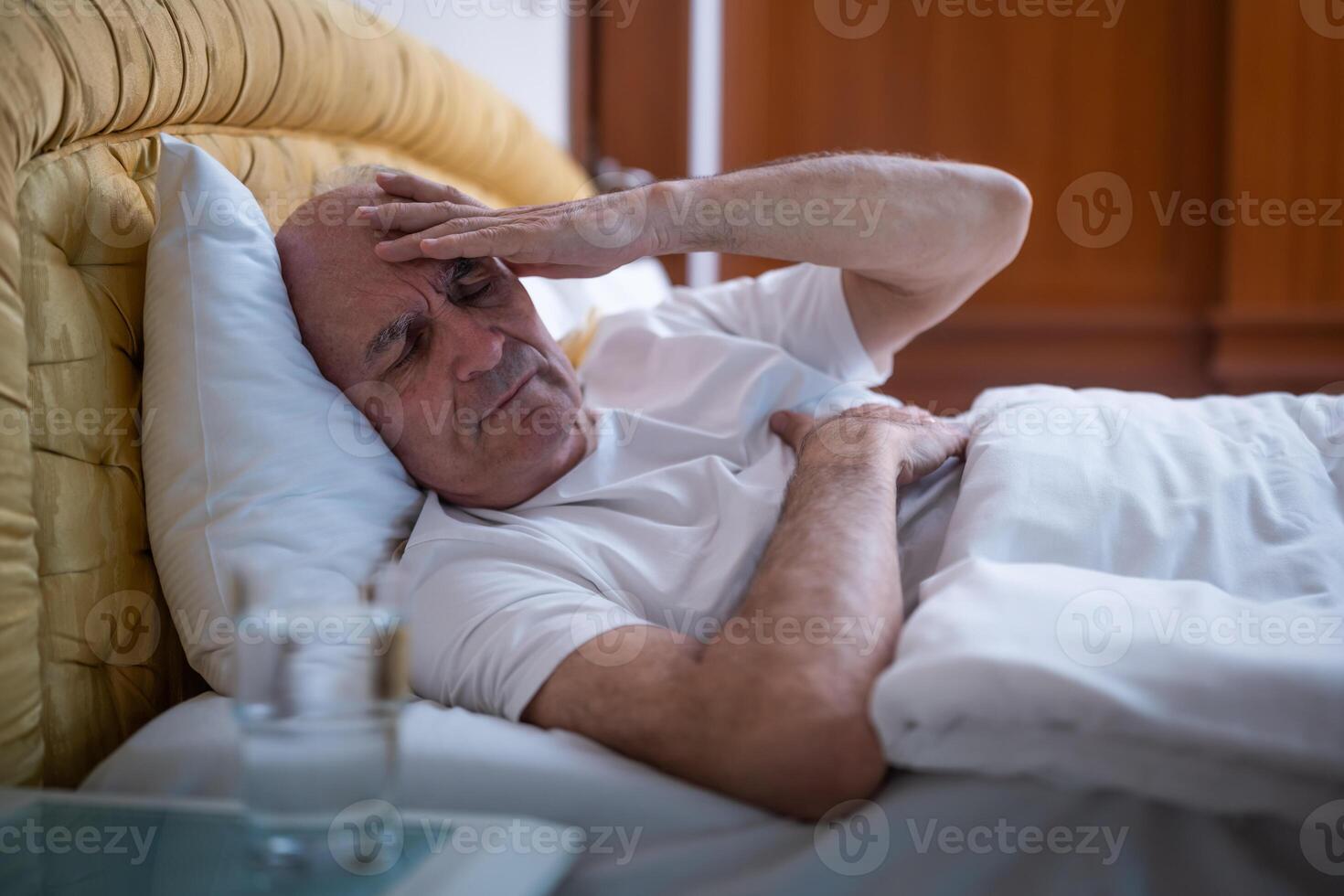 Senior man suffering from headache, lying awake in bed during early morning hours. photo