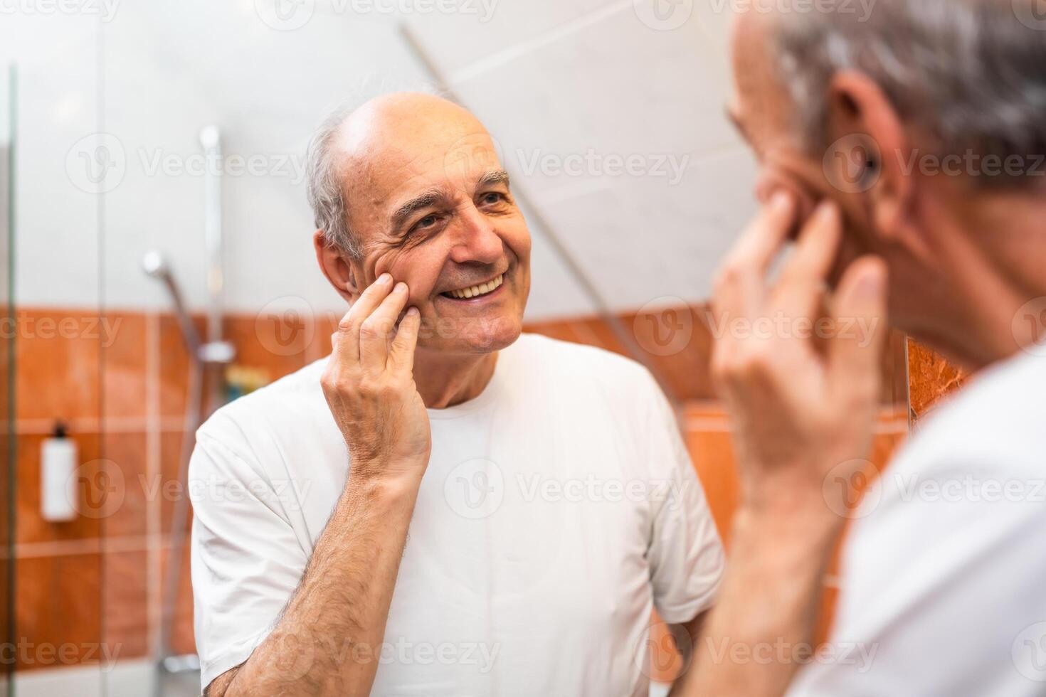 Aged man looking at his reflection in bathroom mirror with happiness, showing the natural aging process with pride. photo