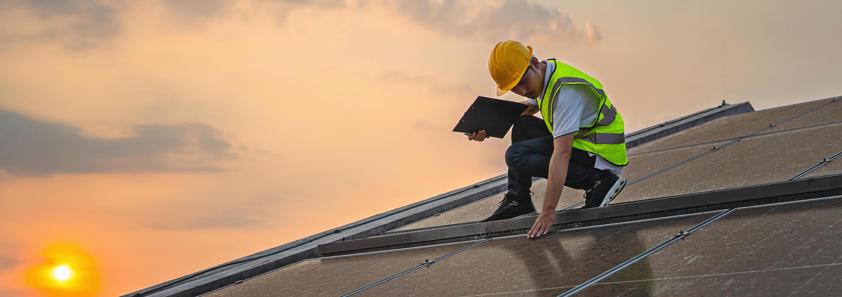 man in a yellow safety vest is looking at a laptop while standing on a roof photo