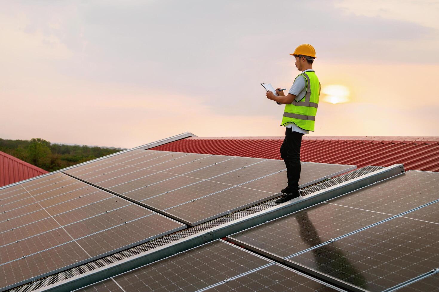 man in a safety vest is standing on a roof, looking at a tablet photo