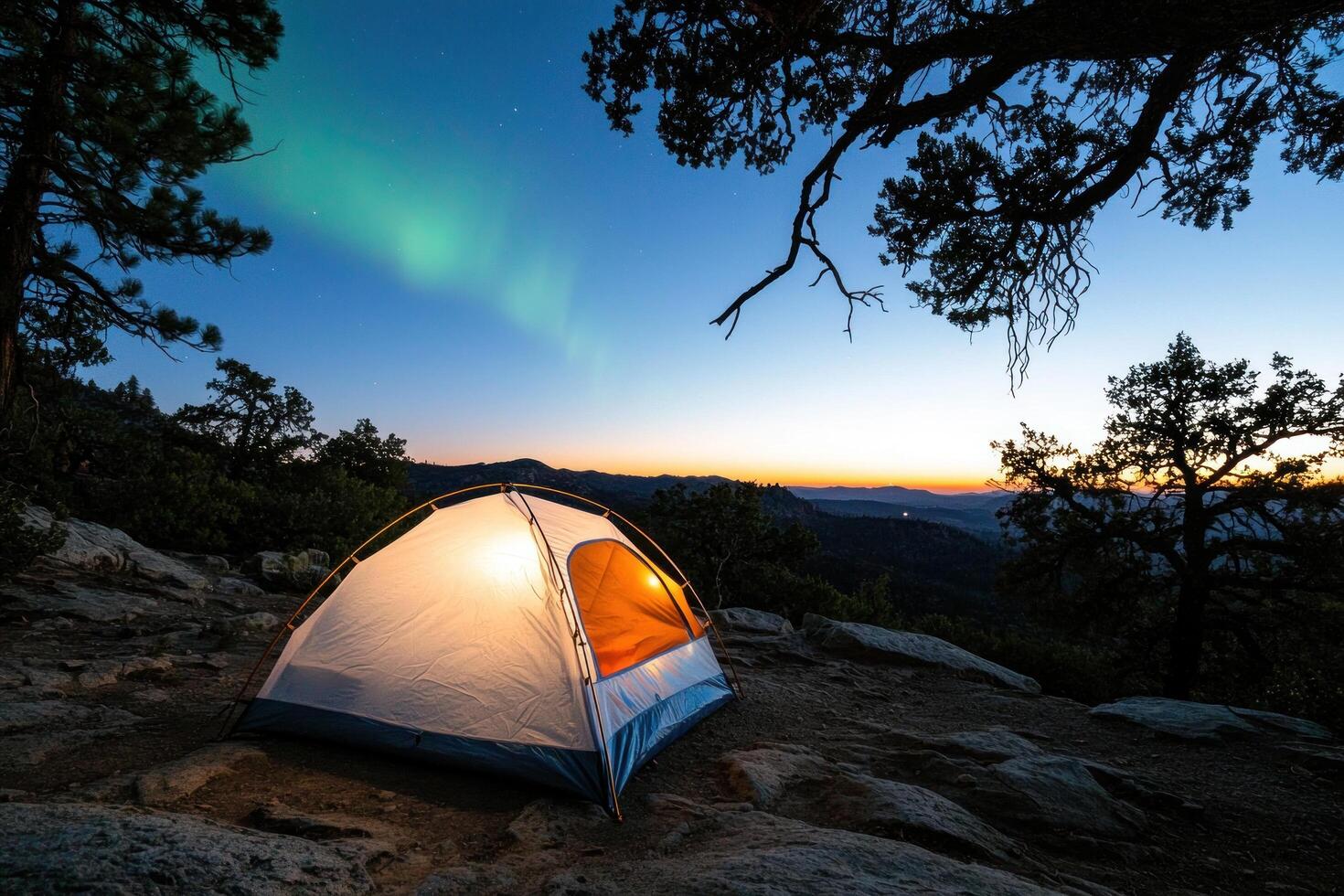 Illuminated tent on mountaintop at sunset under aurora borealis photo