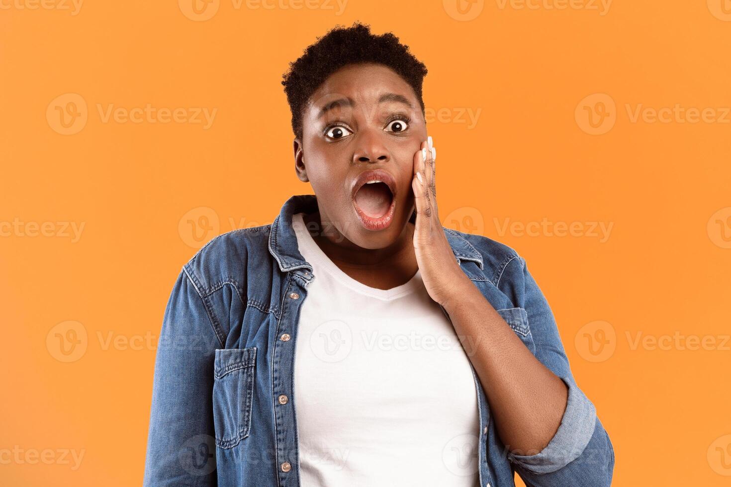 Omg. Shocked Plus Size African American Woman Looking At Camera In Surprise Holding Hand Near Open Mouth Posing Standing Over Yellow Studio Background. Emotional Portrait Concept photo