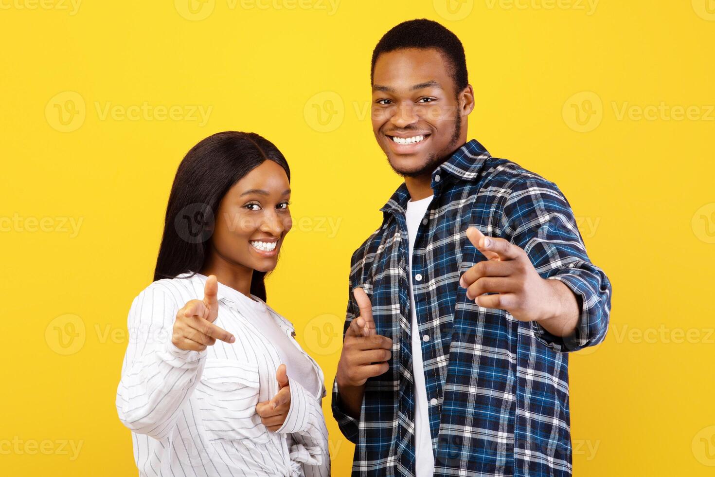 Your turn, you are cool and challenge. Happy excited millennial african american students man and lady in casual show fingers at camera, isolated on yellow background, empty space, studio shot photo
