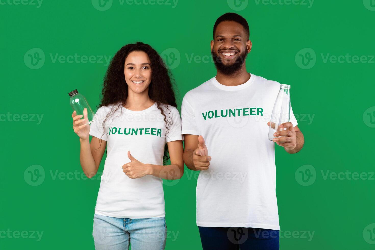 Two Diverse Volunteers Holding Plastic And Glass Bottles Gesturing Like Approving Usage Of Reusable Bottle Standing Posing Over Green Studio Background. Ecology And Consumerism Concept photo