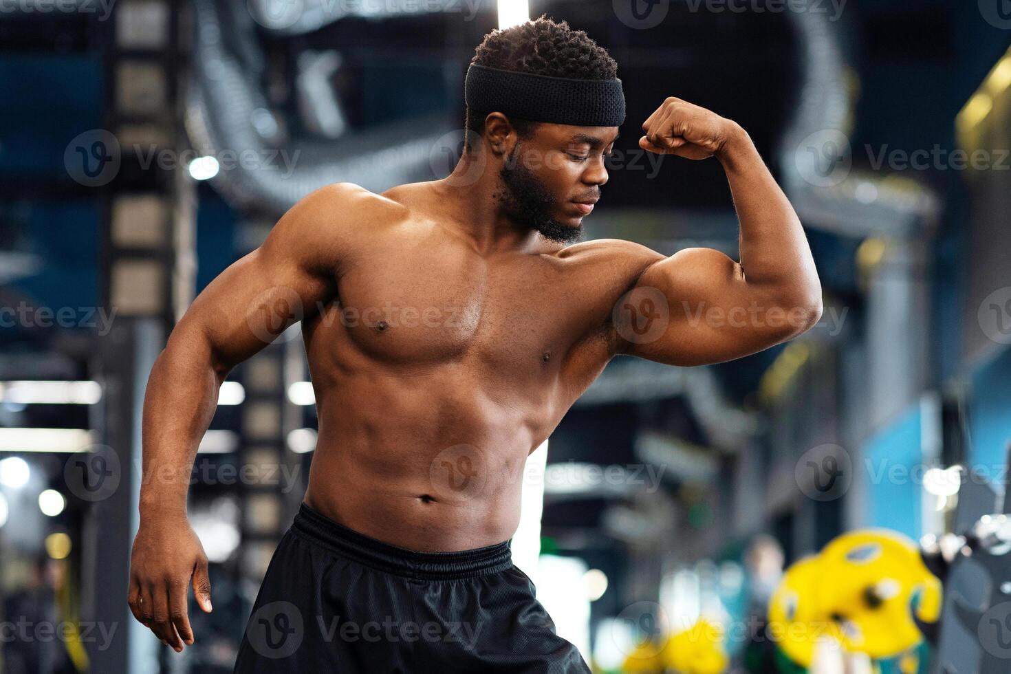 Hot muscular black shirtless man playing with arm muscles in gym, demonstrating his strong biceps, copy space. Bodybuilding, powerlifting, health, fitness, active lifestyle concept photo