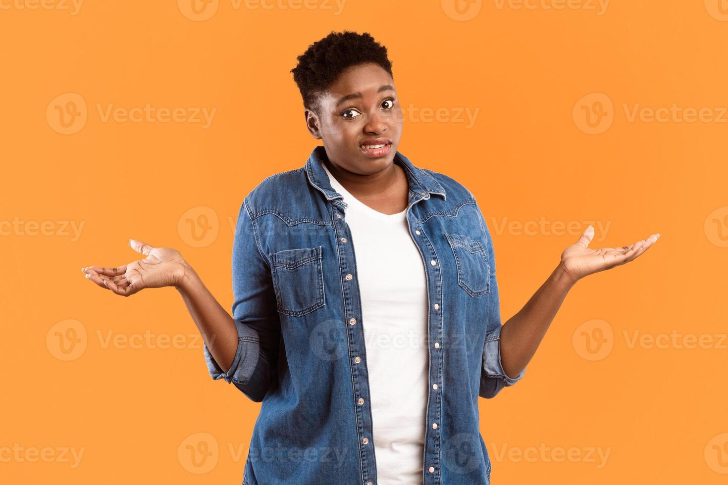 I Don't Know. Puzzled Plus-Size Black Woman Shrugging Shoulders Standing Posing Over Yellow Studio Background, Looking At Camera. Shoulder Shrug Gesture Concept. photo