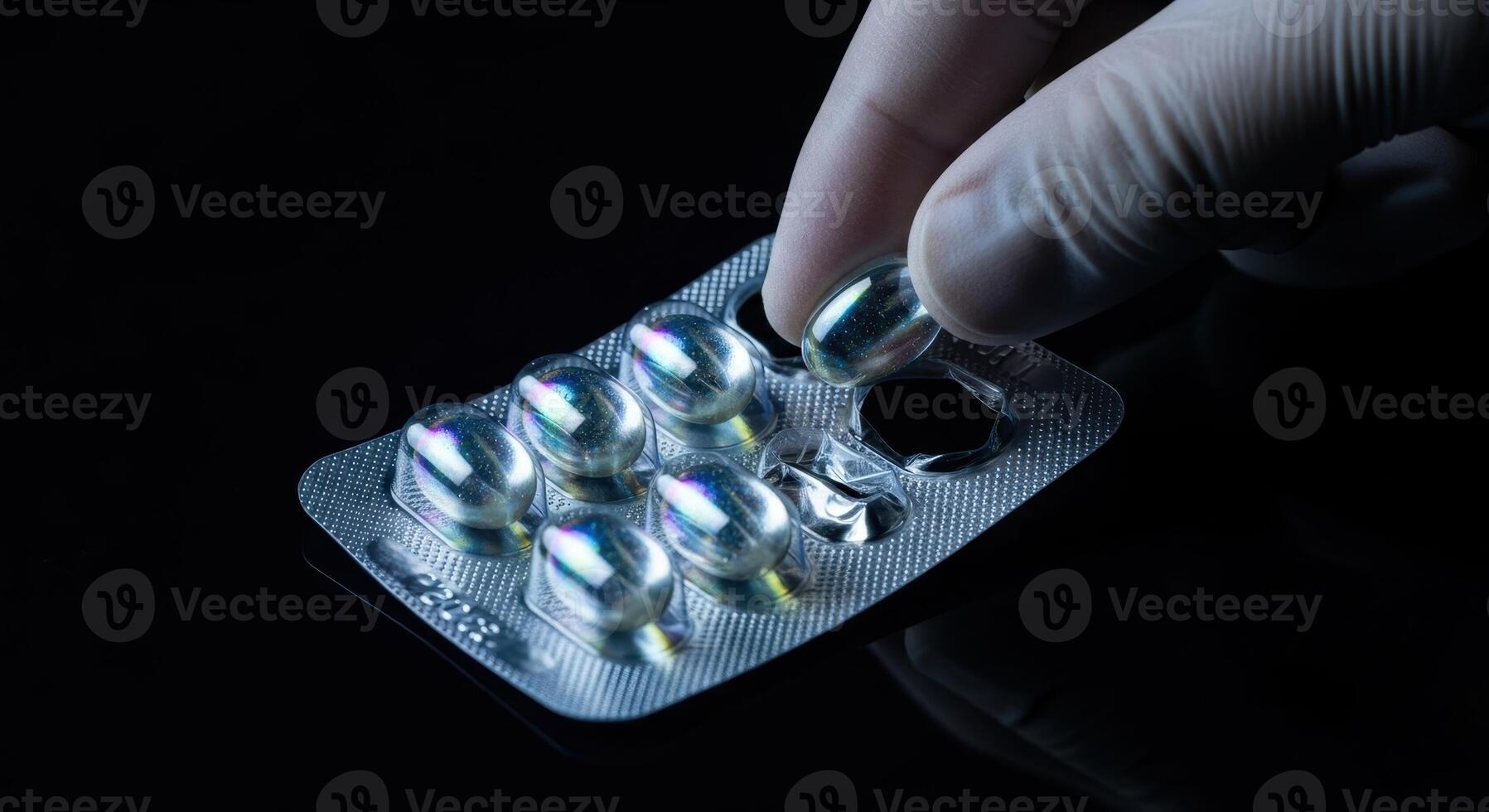 Hand in glove taking shimmering iridescent capsule from blister pack against dark background photo