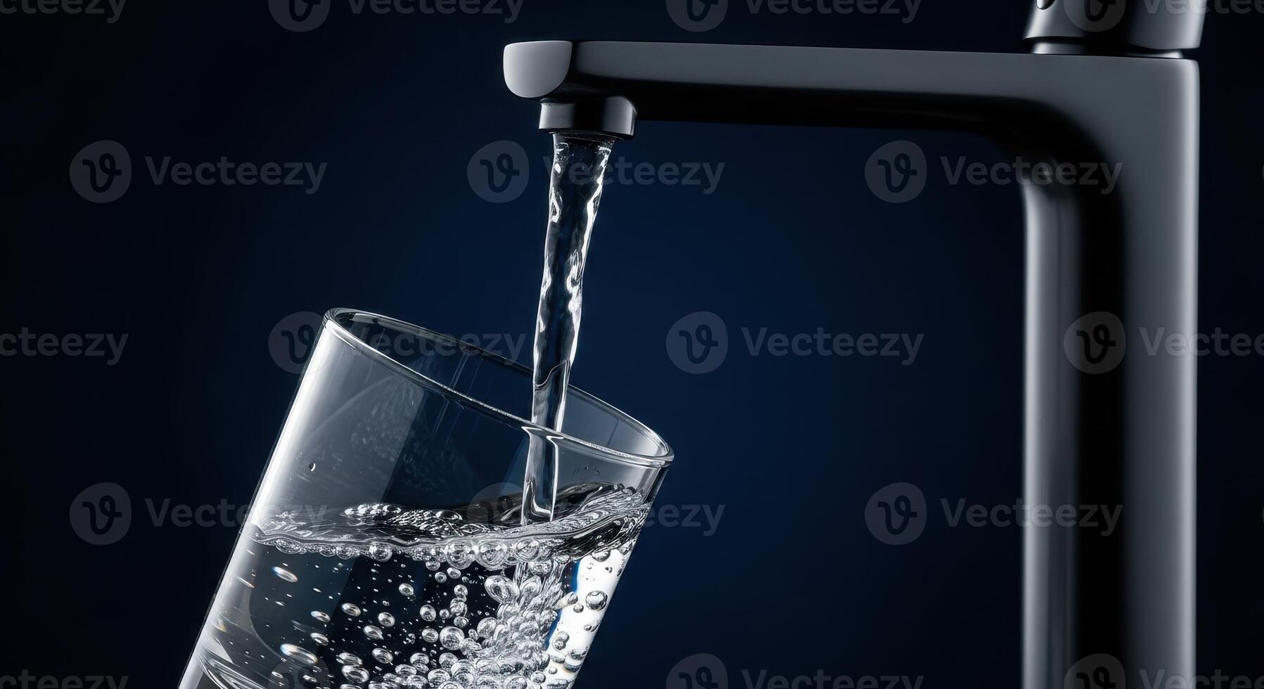 Fresh water pouring from a modern black faucet into a clear drinking glass photo