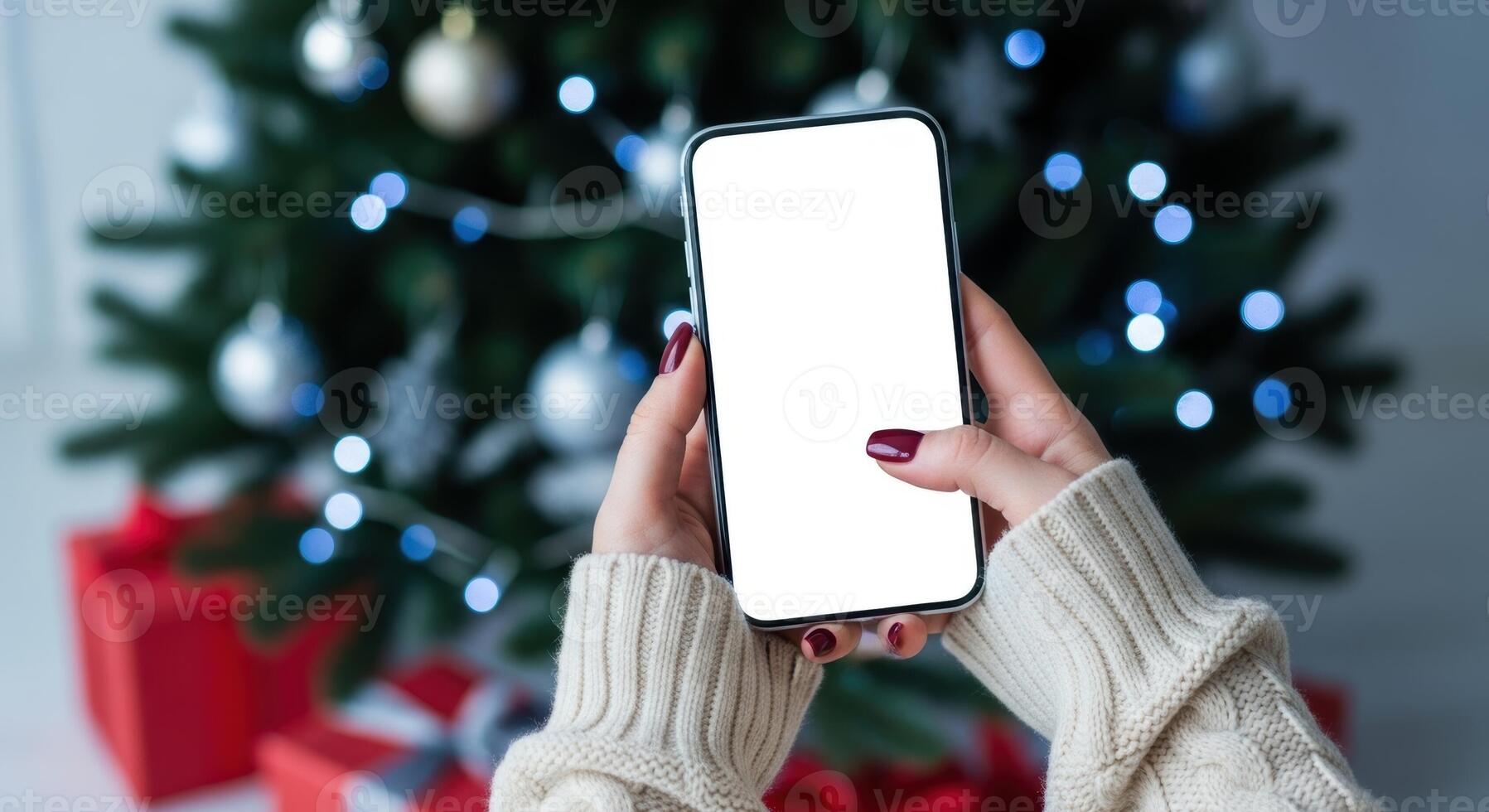 Woman holding a smartphone with blank white screen in front of a christmas tree. photo