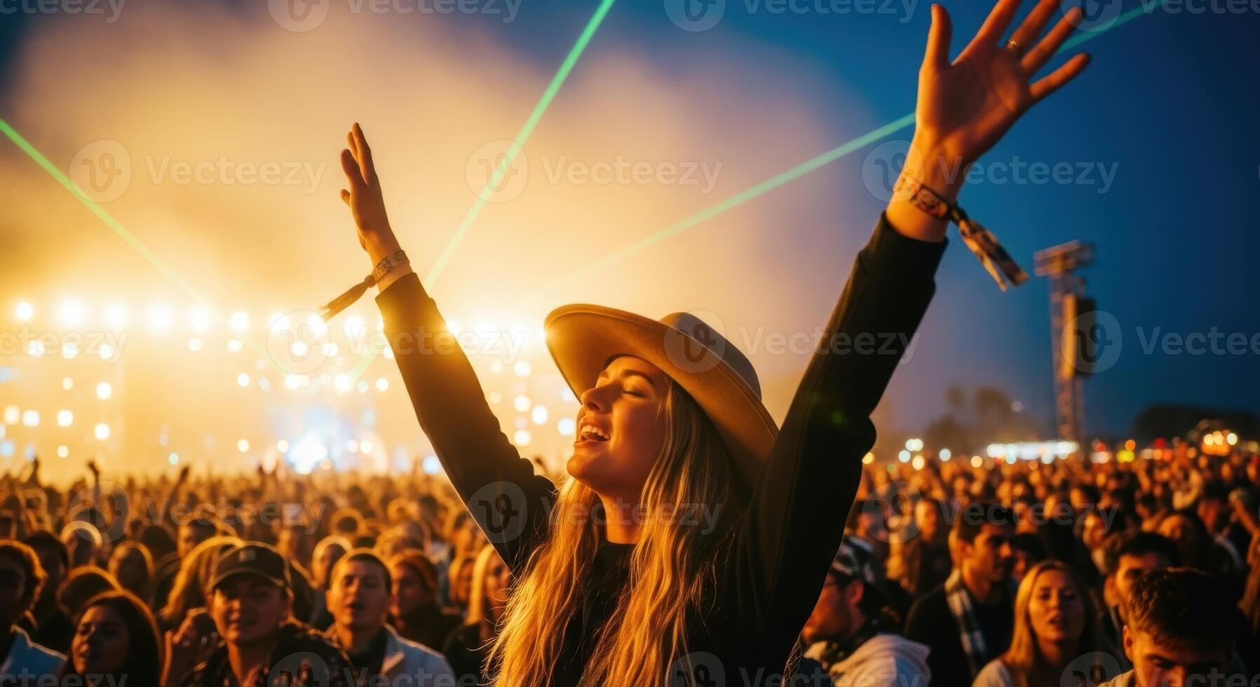 Young woman with a cowboy hat enjoying a vibrant live music concert with arms raised in a cheering crowd. photo