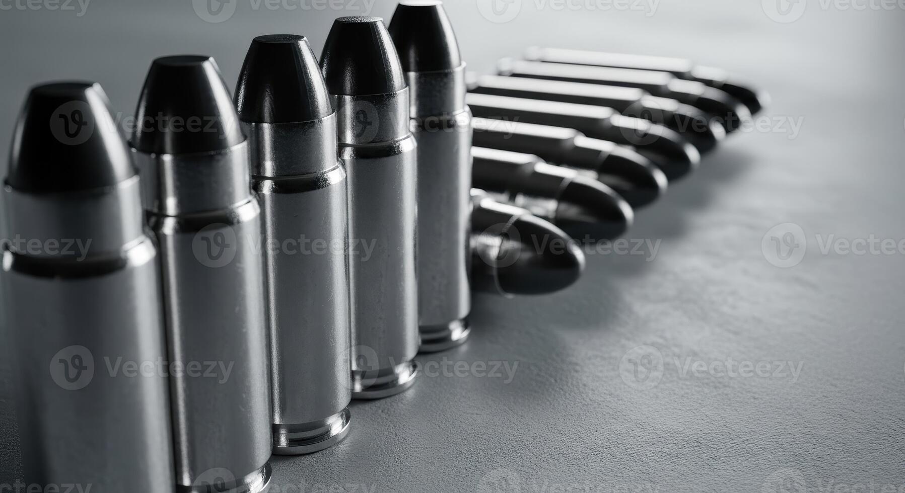 Close up of a row of shiny silver bullets arranged diagonally on a grey surface. photo