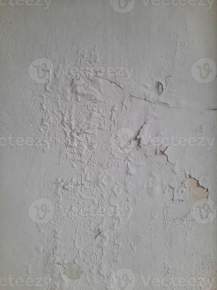 Old peeling wall texture with cracked, blistered, and flaking white paint, creating a weathered and distressed surface look. photo