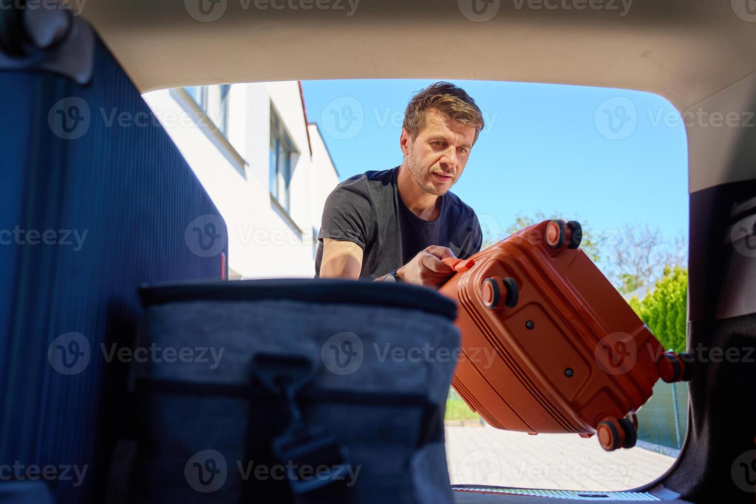 Man loading suitcase into car trunk before travel photo