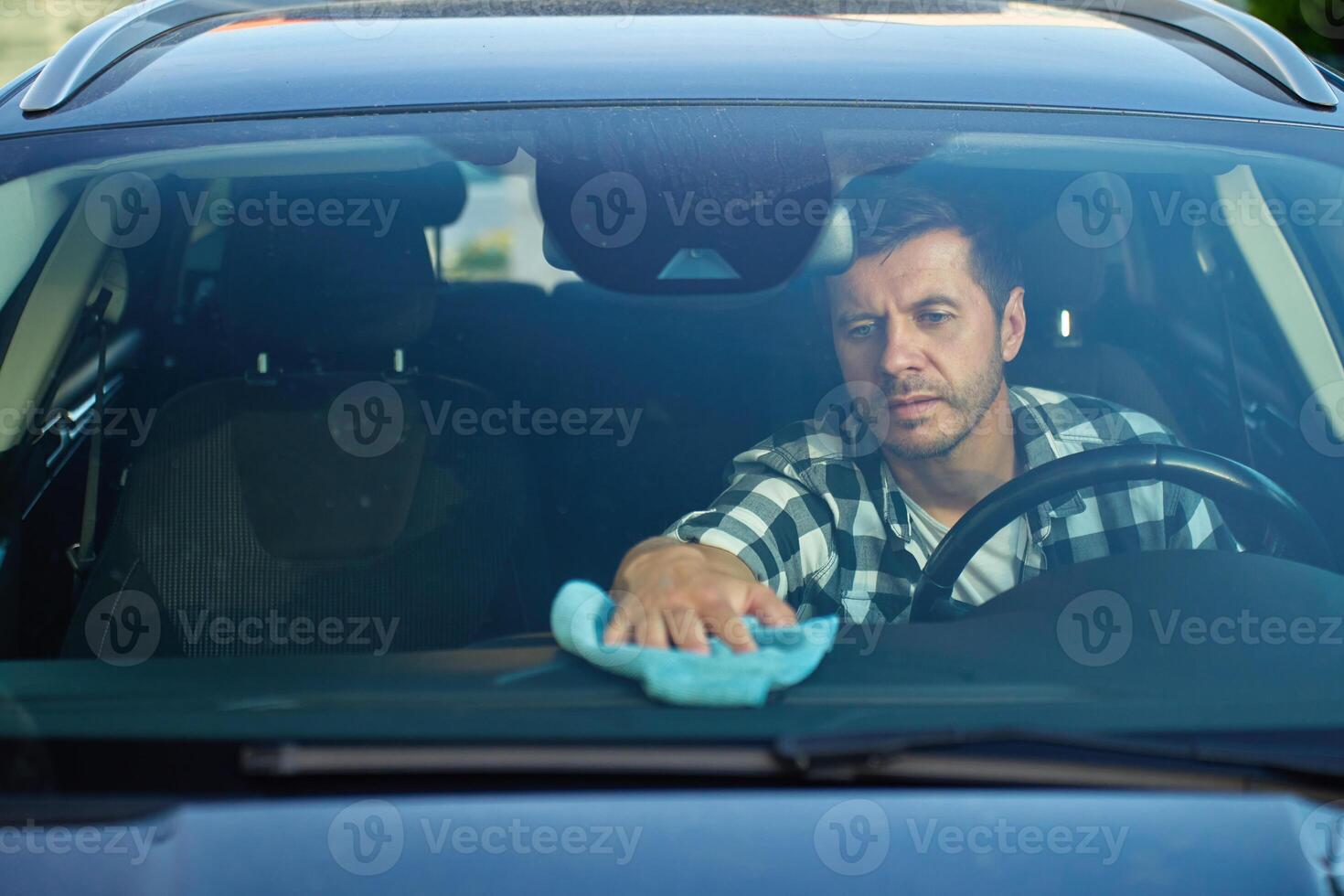 Man cleaning car dashboard from inside of car photo