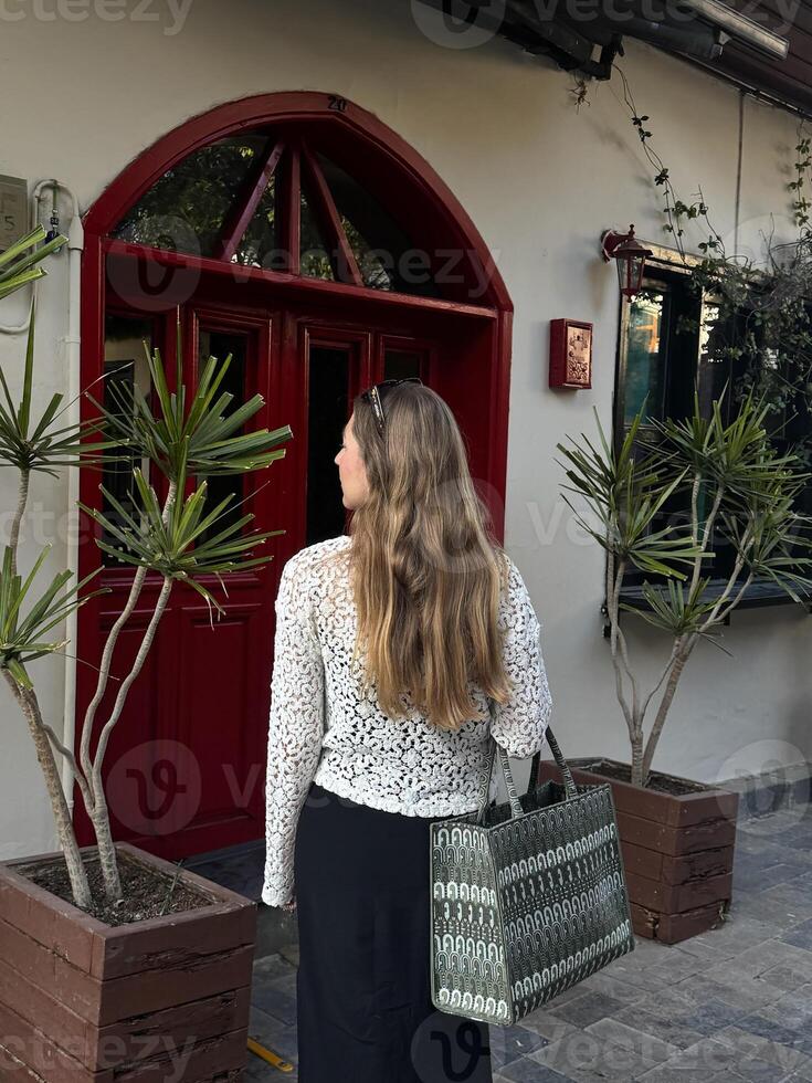 A woman stands outside a quaint building with red doors, admiring the surroundings photo
