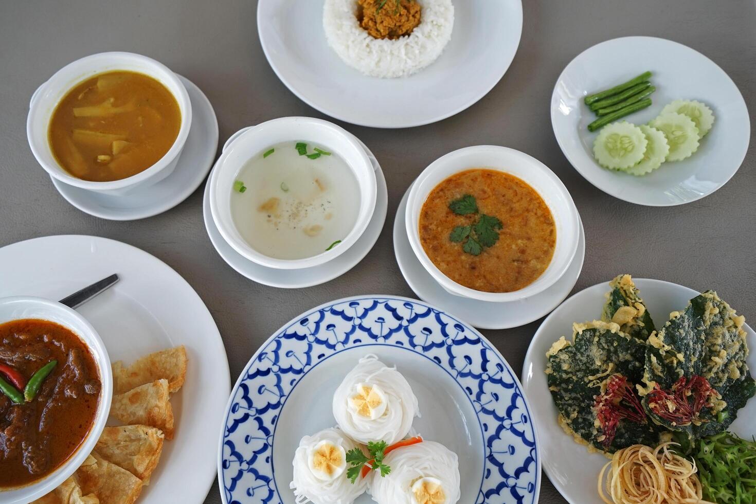 Close up Thai Vermicelli rice noodle served with sweet and sour peanut sauce, deep fried wild Betal leafbush, Stir fry pork with spicy southern Thai style paste, stew beef curry with crispy Roti photo