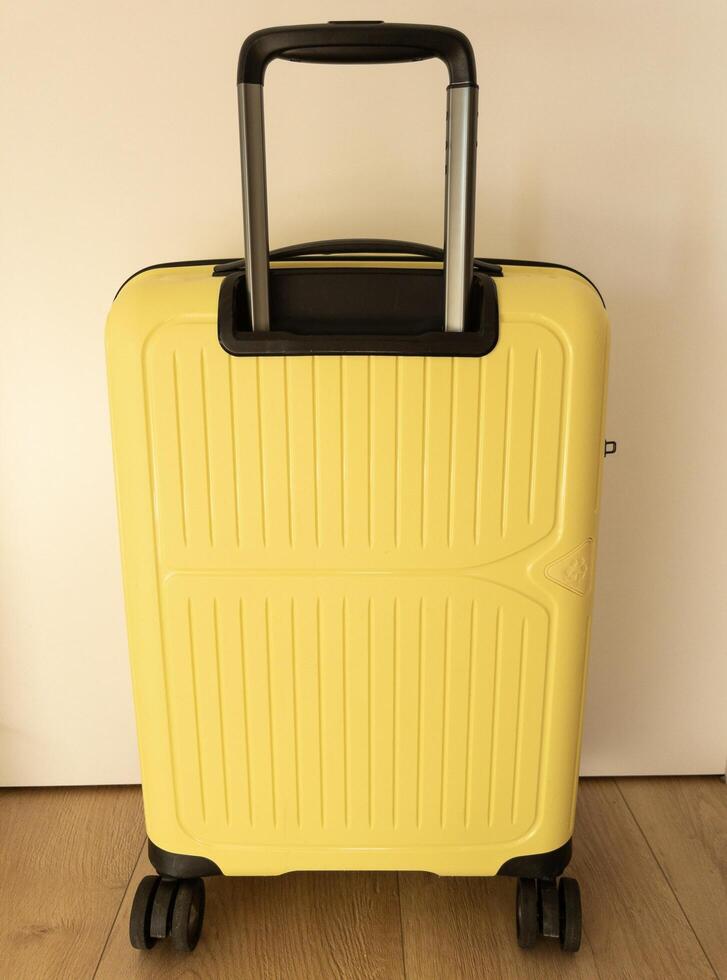 A bright yellow suitcase with sunglasses stands near a white wall photo