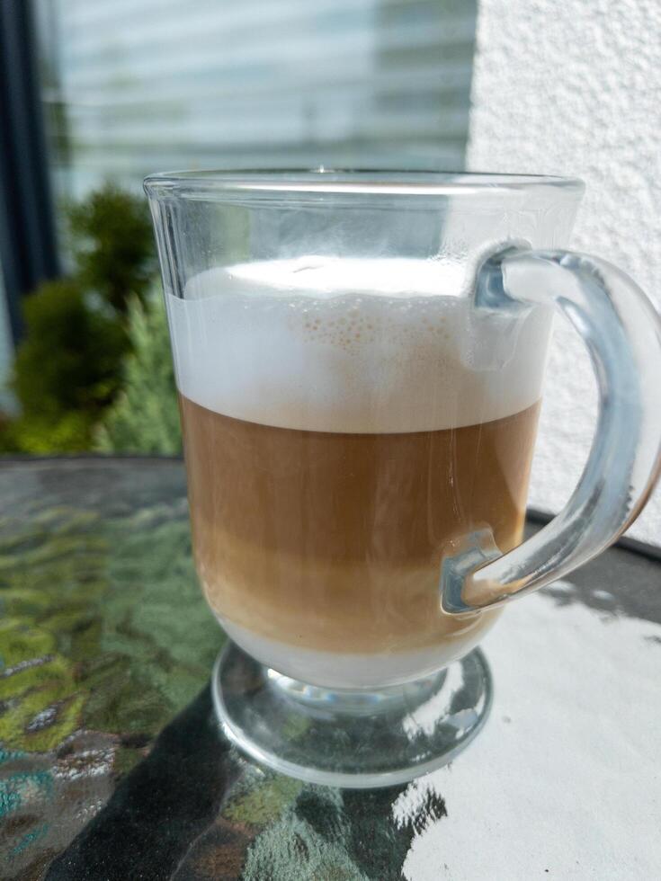 A cup of coffee drink, cappuccino, latte or mocha with milk foam. Glass transparent mug, outdoors photo